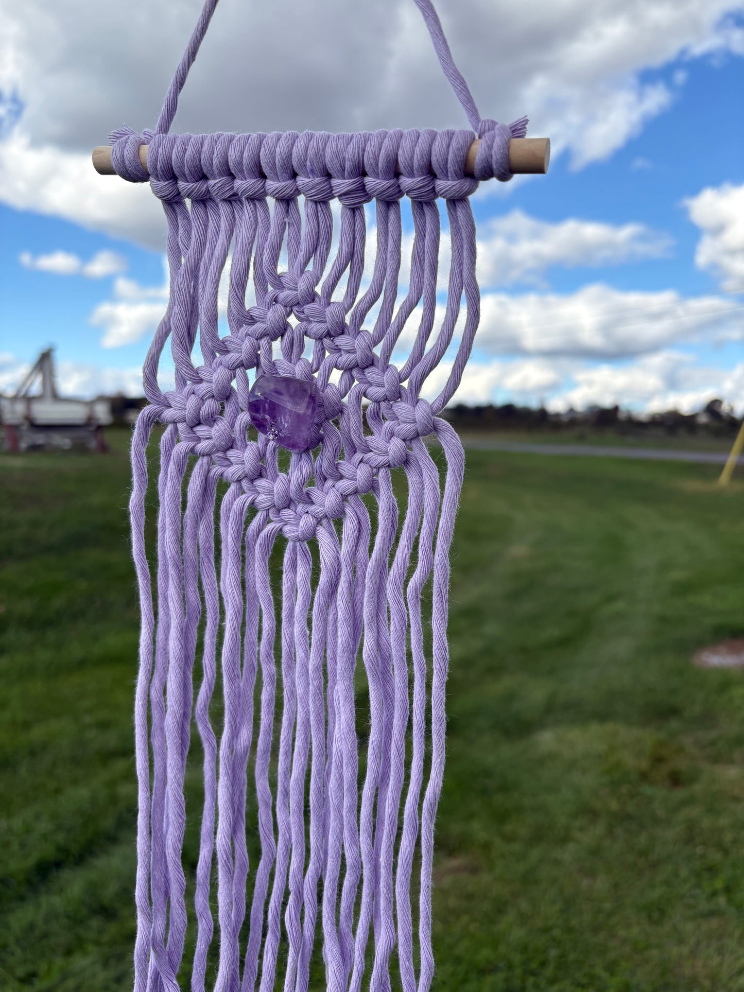 Macrame wall hanging with purple threads against a blurred natural background